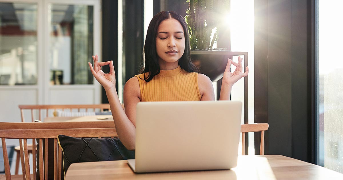 Woman sitting at laptop in a yoga pose.